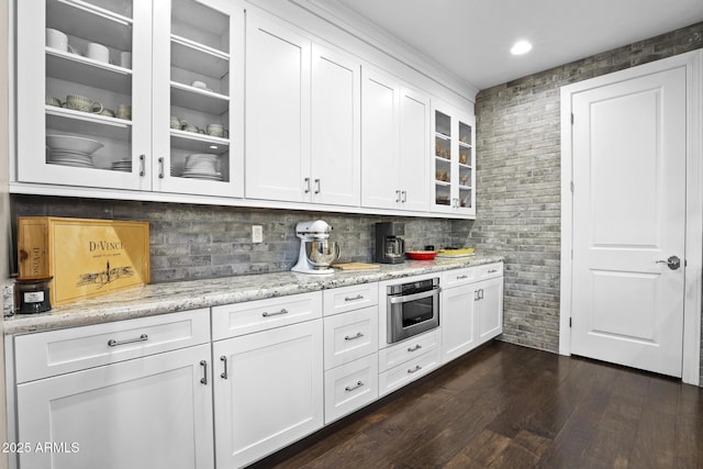 kitchen featuring light stone counters, oven, white cabinetry, dark wood finished floors, and glass insert cabinets