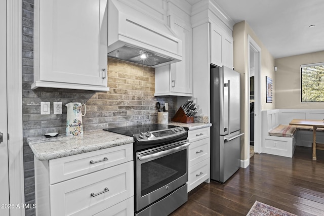 kitchen with stainless steel appliances, decorative backsplash, white cabinets, light stone countertops, and premium range hood