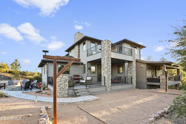 back of property featuring an outdoor fire pit, a patio, a balcony, stone siding, and a chimney