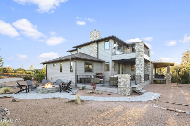 back of property featuring an outdoor fire pit, a balcony, a shingled roof, a chimney, and a patio area