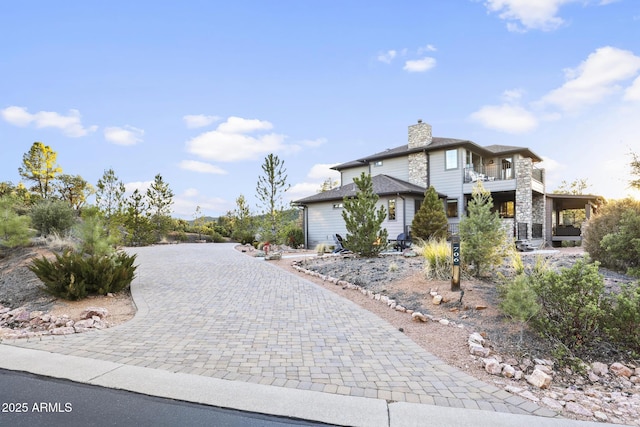 view of front of home featuring decorative driveway, a chimney, and a balcony