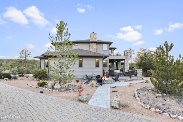 back of house with a shingled roof, a fire pit, a patio, a balcony, and a chimney