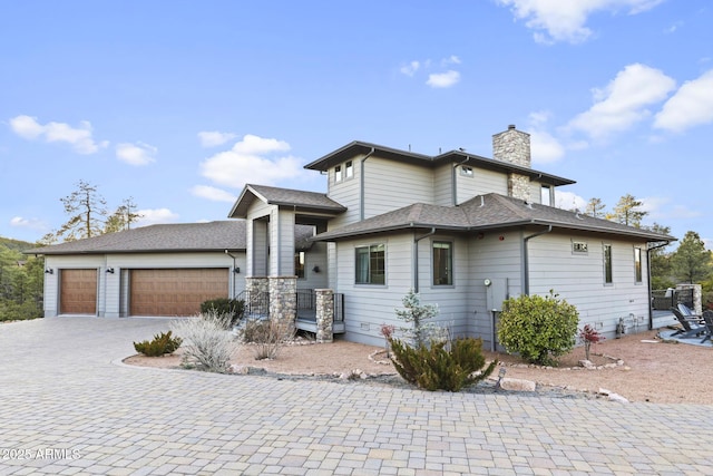 prairie-style home with roof with shingles, driveway, a chimney, and an attached garage