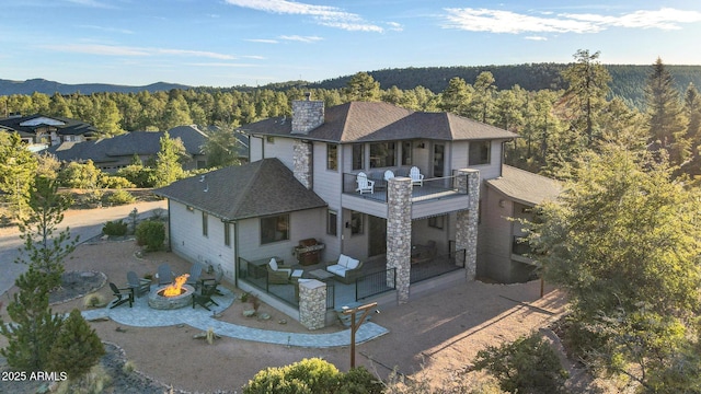 view of front of home with an outdoor fire pit, a balcony, a shingled roof, a chimney, and a wooded view