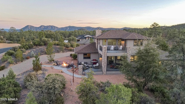 back of property at dusk with a fire pit, a balcony, a chimney, a patio area, and a mountain view