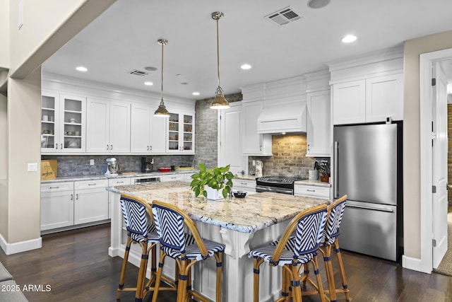 kitchen with glass insert cabinets, custom range hood, appliances with stainless steel finishes, and light stone counters