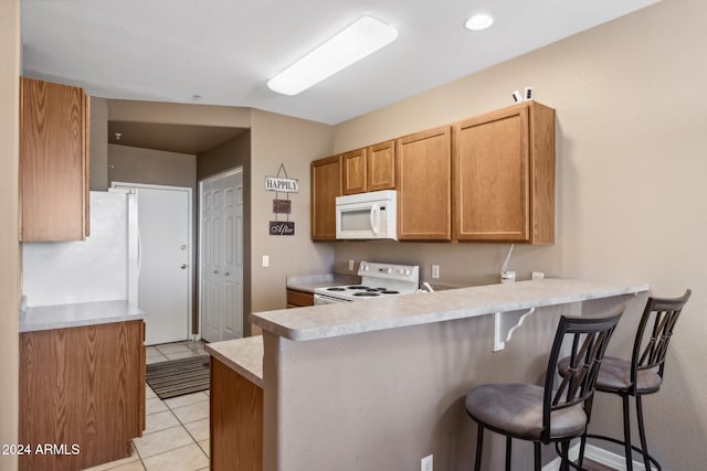 kitchen featuring white appliances, kitchen peninsula, light tile patterned floors, and a kitchen bar