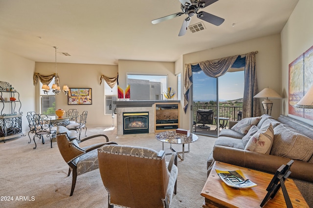 living area featuring carpet floors, ceiling fan with notable chandelier, visible vents, and a premium fireplace