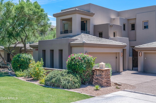 pueblo-style house with stucco siding, a front yard, a garage, driveway, and a tiled roof