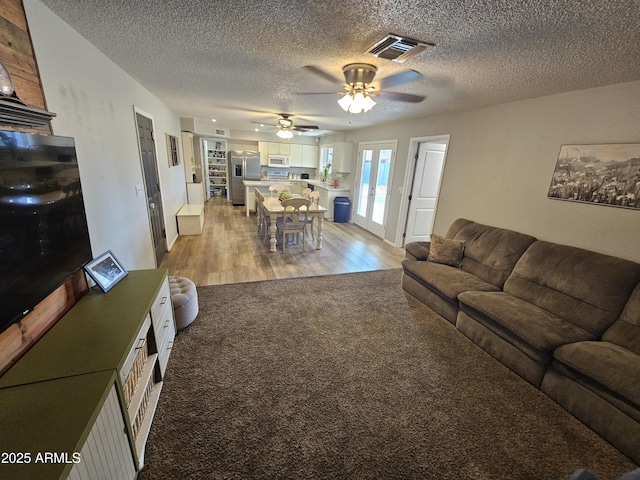 living room with visible vents, light carpet, a textured ceiling, a ceiling fan, and light wood-style flooring