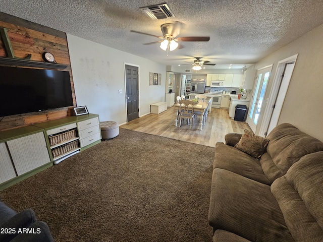 living area with ceiling fan, light carpet, light wood finished floors, a textured ceiling, and visible vents