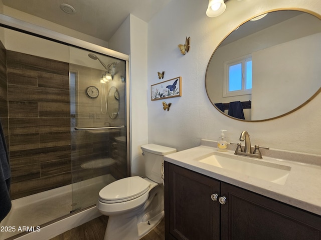 bathroom with vanity, toilet, wood finished floors, and a stall shower