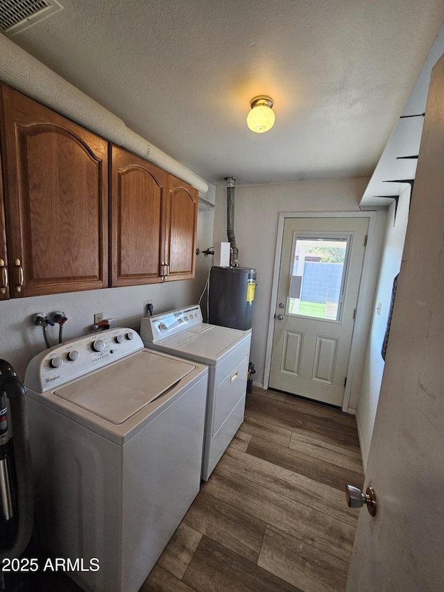 laundry area with visible vents, dark wood-type flooring, washing machine and clothes dryer, cabinet space, and water heater
