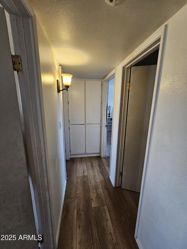 hall with a textured ceiling and wood finished floors