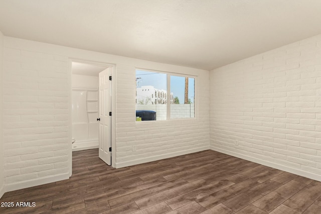 spare room with brick wall and dark wood-type flooring