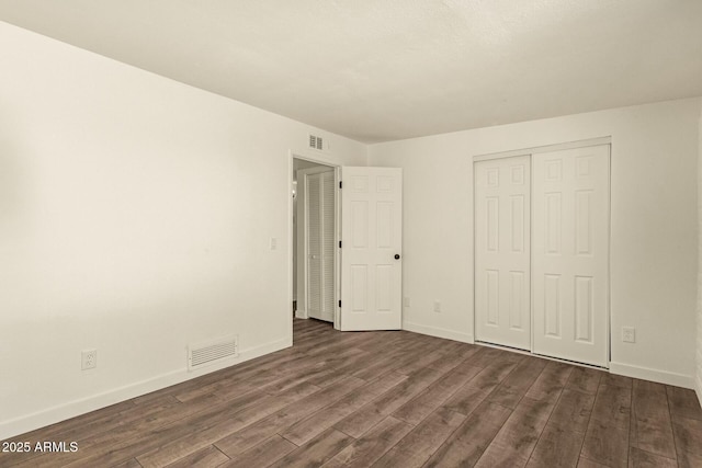 unfurnished bedroom featuring a closet, dark wood-style flooring, visible vents, and baseboards