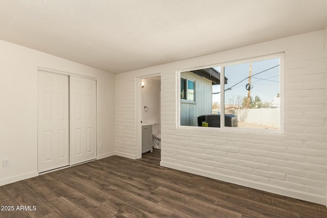 interior space with brick wall, baseboards, and dark wood-style flooring