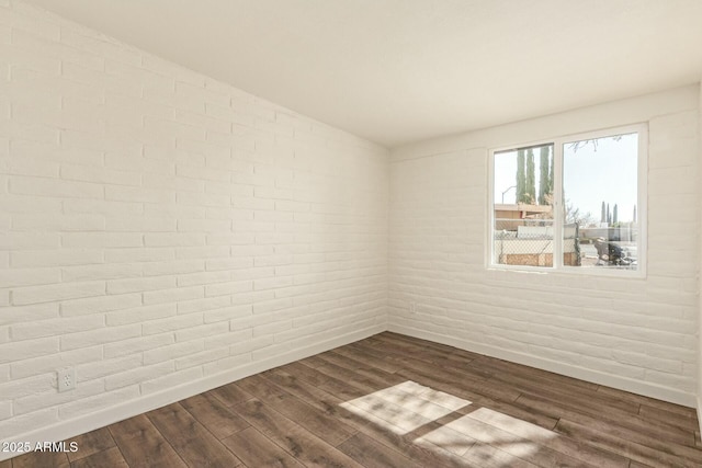 spare room with brick wall, baseboards, and dark wood-style flooring