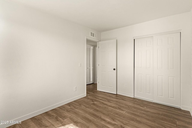 unfurnished bedroom featuring a closet, visible vents, baseboards, and wood finished floors