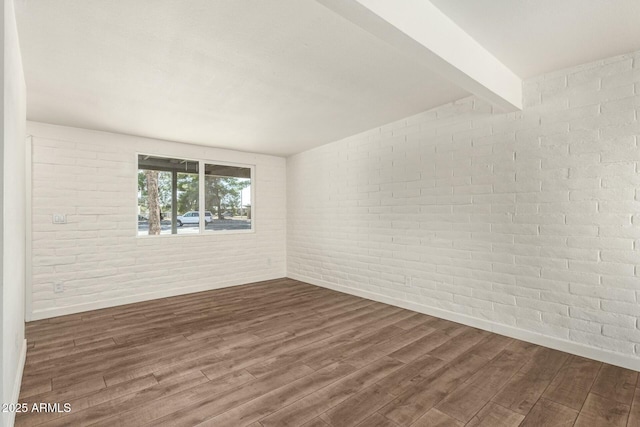 spare room featuring brick wall, beamed ceiling, and dark wood finished floors