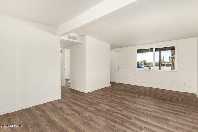 spare room featuring visible vents, baseboards, dark wood-style floors, brick wall, and beamed ceiling