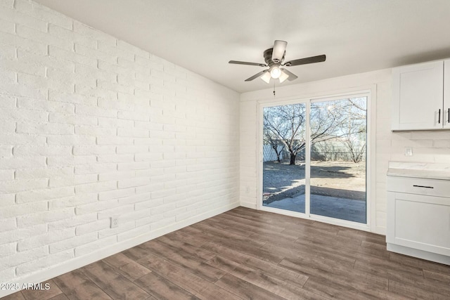 unfurnished dining area featuring ceiling fan, brick wall, dark wood-type flooring, and baseboards