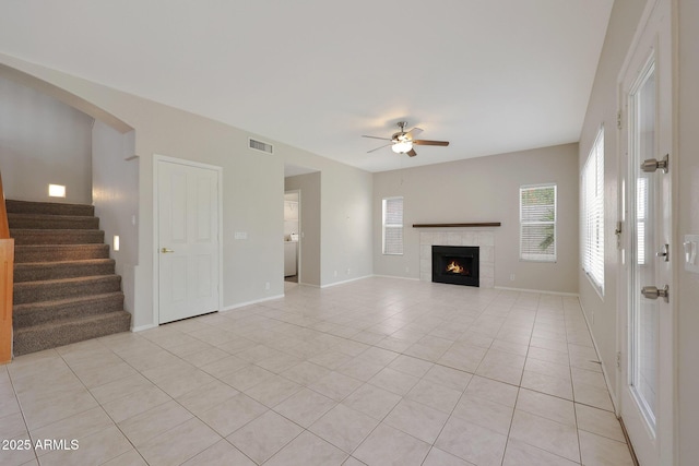 unfurnished living room with a tiled fireplace, light tile patterned floors, and ceiling fan