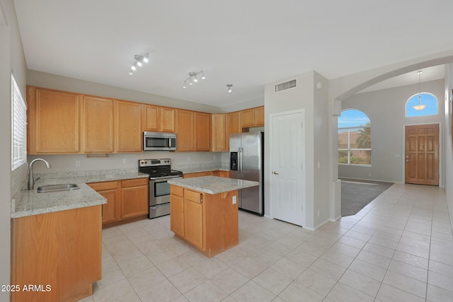 kitchen featuring sink, light tile patterned floors, appliances with stainless steel finishes, a center island, and light stone counters