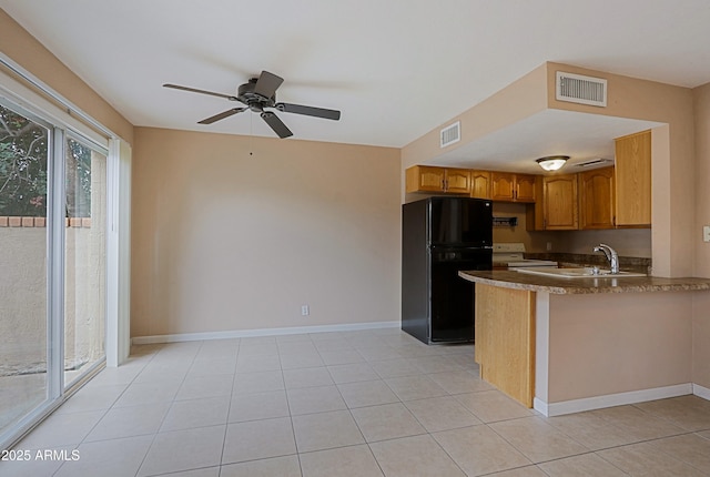 kitchen featuring visible vents, baseboards, white range with electric stovetop, freestanding refrigerator, and brown cabinetry