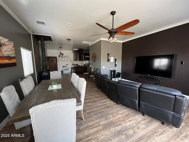 dining room featuring visible vents, a ceiling fan, ornamental molding, light wood-type flooring, and a wood stove