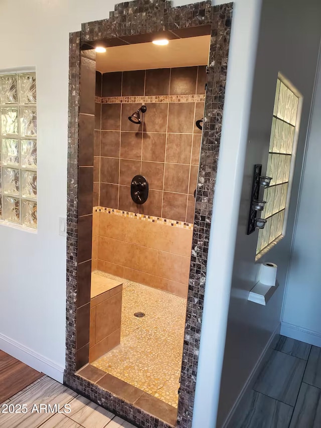 bathroom with wood finish floors, tiled shower, and baseboards