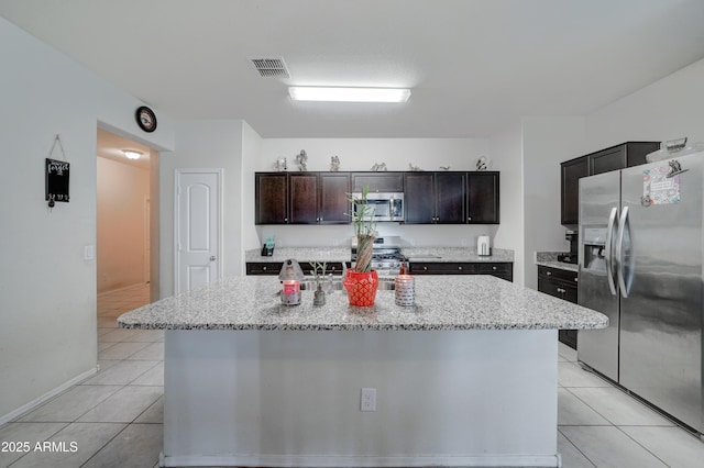 kitchen with stainless steel appliances, light stone countertops, dark brown cabinets, and a kitchen island with sink