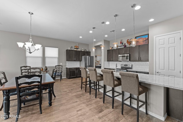4244 Sawbuck Way, Wickenburg, AZ 85390 - kitchen featuring a kitchen breakfast bar, stainless steel appliances, a chandelier, backsplash, and light wood-style floors