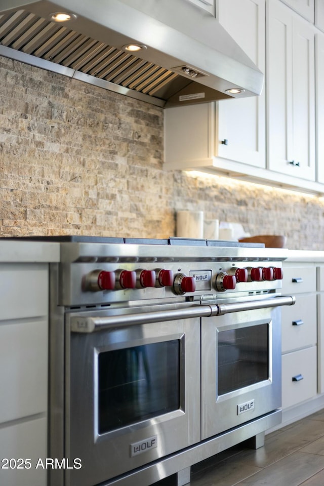 kitchen with range hood, white cabinetry, and range with two ovens