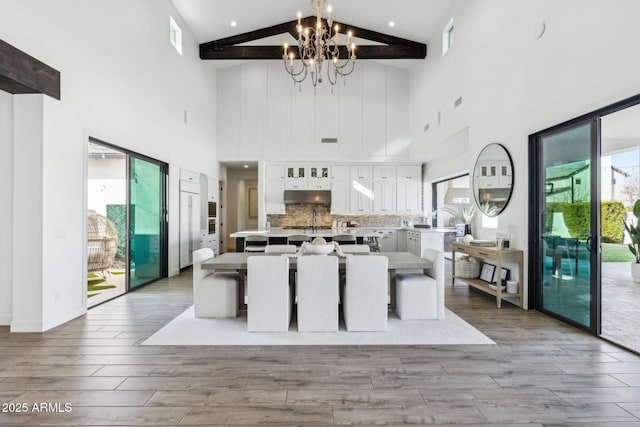 kitchen featuring wood finished floors, a kitchen island with sink, light countertops, under cabinet range hood, and white cabinetry