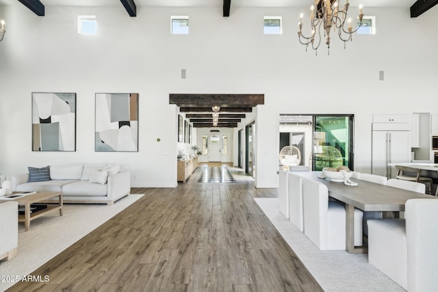 living room featuring a wealth of natural light, a notable chandelier, beamed ceiling, and wood finished floors