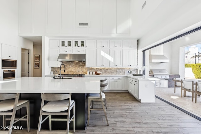 kitchen featuring black microwave, tasteful backsplash, visible vents, under cabinet range hood, and stainless steel oven