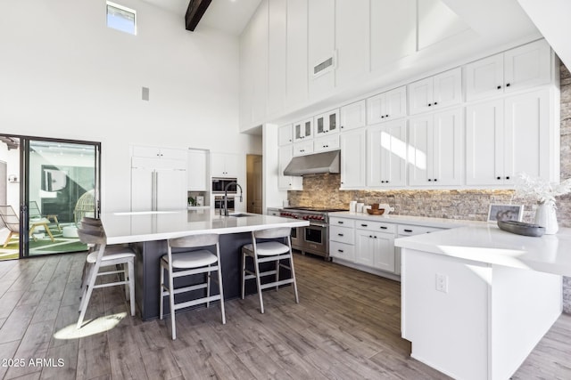 kitchen featuring a breakfast bar area, visible vents, white cabinetry, built in appliances, and under cabinet range hood