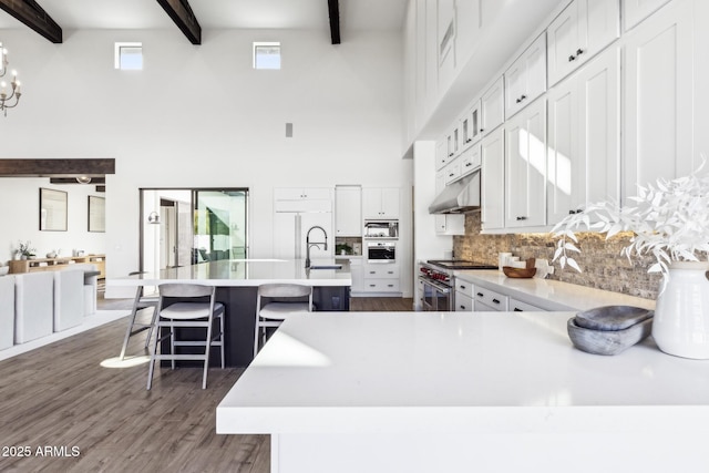 kitchen with dark wood-style floors, light countertops, built in appliances, beamed ceiling, and under cabinet range hood