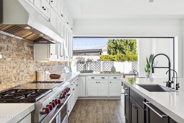 kitchen with double oven range, a sink, light countertops, and under cabinet range hood