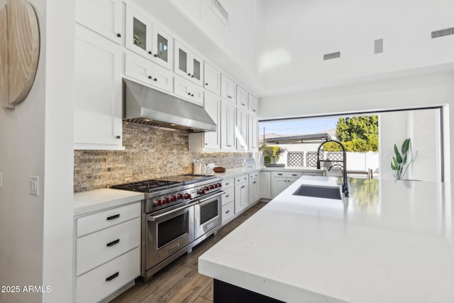 kitchen with backsplash, white cabinets, a sink, double oven range, and under cabinet range hood