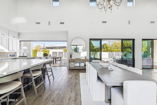 dining space featuring light wood-type flooring, an inviting chandelier, a towering ceiling, and visible vents