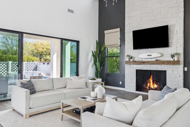 living area with a towering ceiling, a fireplace, visible vents, and wood finished floors