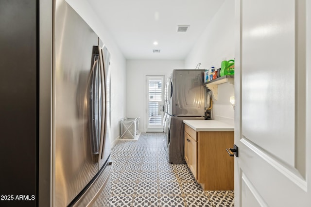 kitchen with visible vents, stacked washer / dryer, brown cabinets, freestanding refrigerator, and light countertops