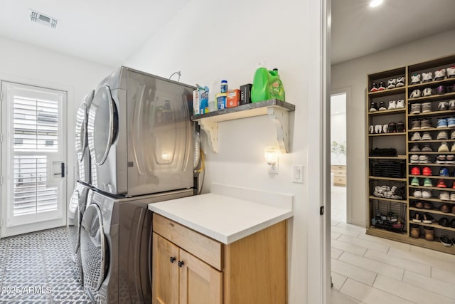 washroom featuring stacked washer and dryer, cabinet space, and visible vents