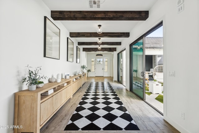 hall with light wood-type flooring, baseboards, visible vents, and beamed ceiling