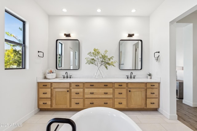 bathroom with a freestanding tub, tile patterned flooring, a sink, baseboards, and double vanity