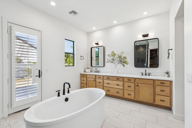 bathroom featuring double vanity, a freestanding tub, visible vents, and recessed lighting