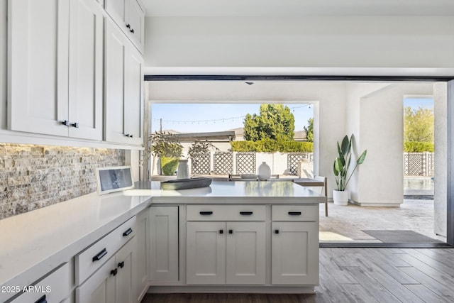 kitchen featuring a peninsula, wood finished floors, white cabinetry, light countertops, and backsplash