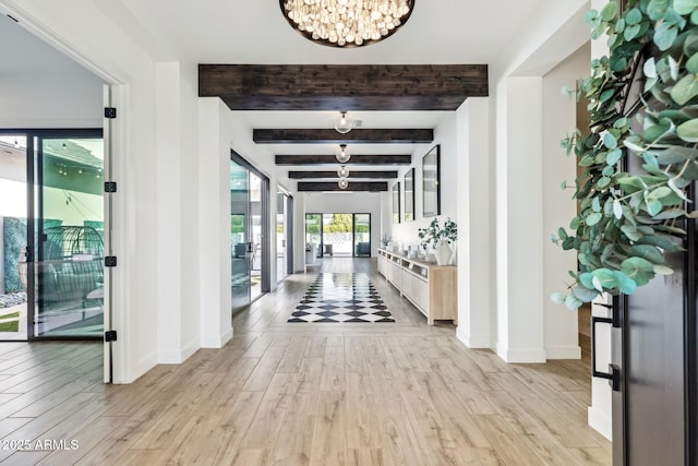 corridor featuring light wood-type flooring, beam ceiling, baseboards, and a notable chandelier